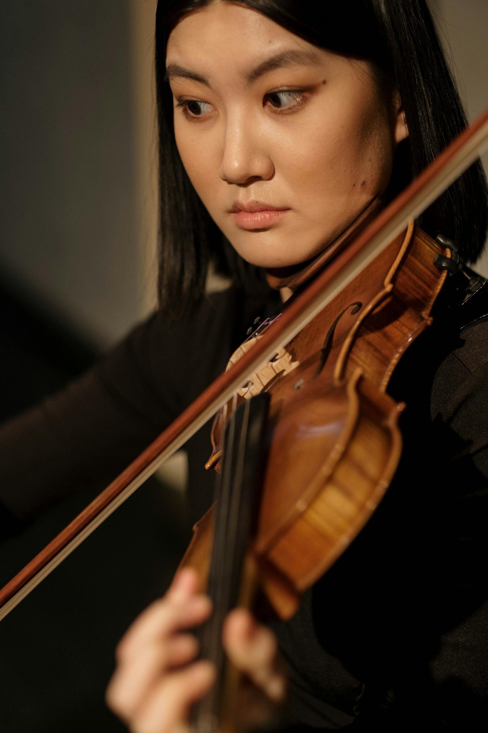 Close-up of an Asian woman passionately playing the violin, focused on her art.